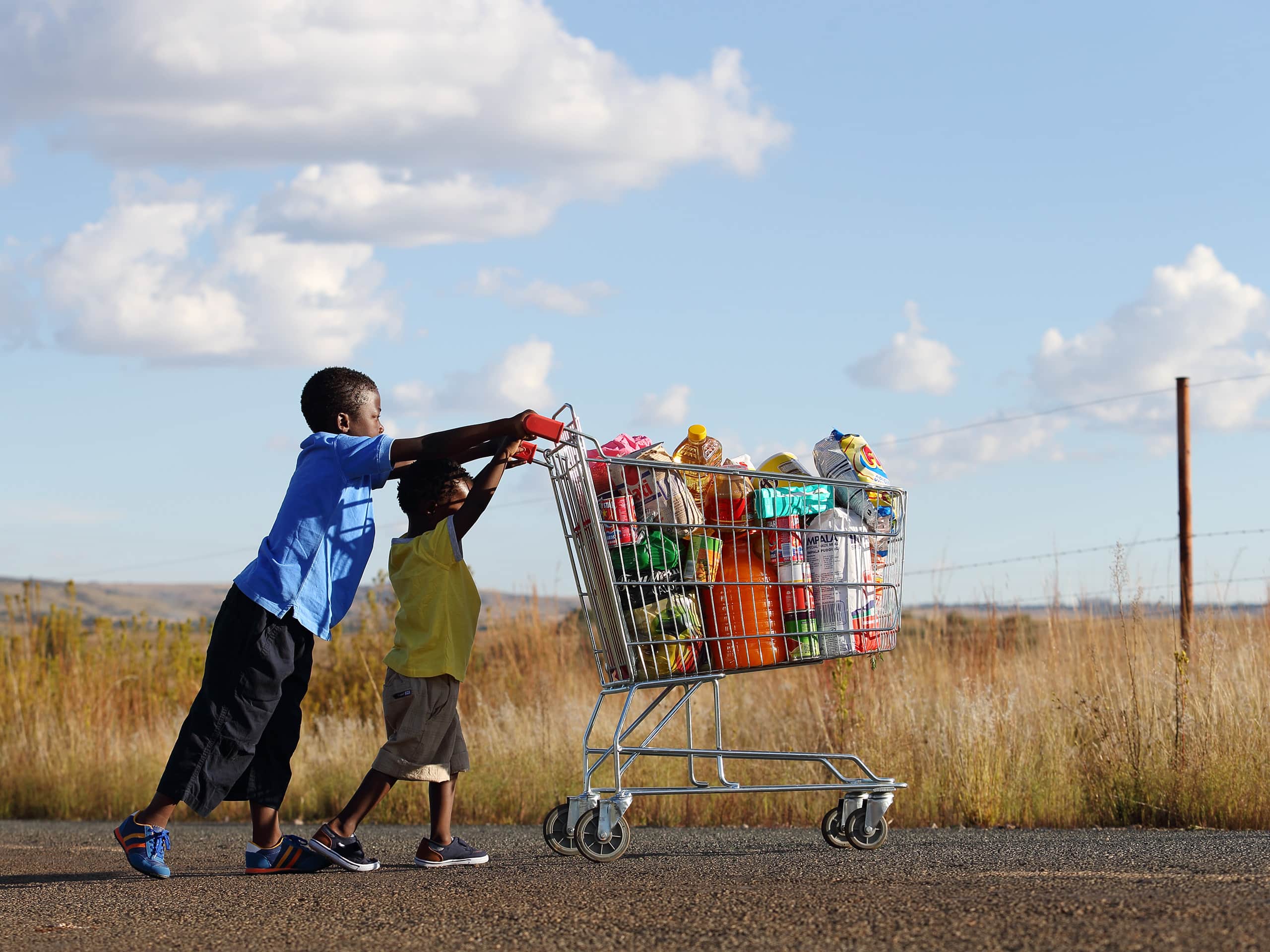 Two small boys pushing a trolley of food along a tarred road. Photograph by Elsa Young. Two small boys pushing a trolley of food along a tarred road. Photograph by Elsa Young.