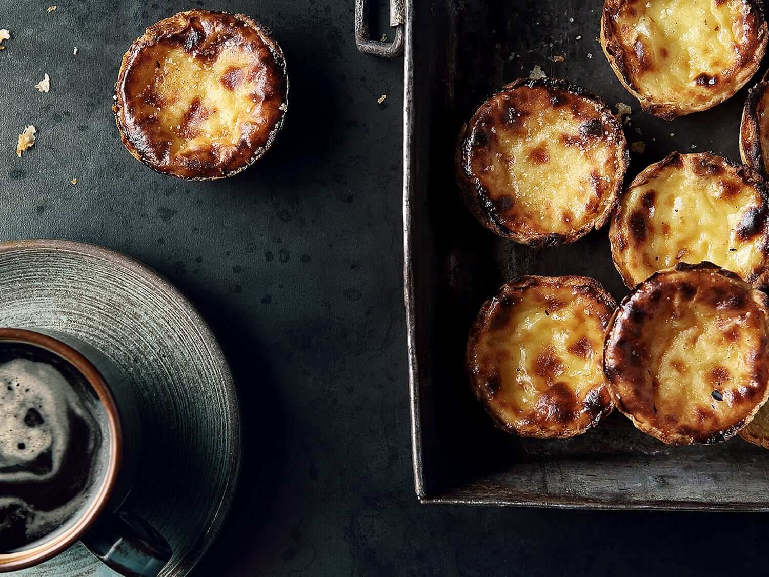 Mouth-watering Pastéis de Nata and a cup of coffee seen from above. Photo by Elsa Young. Mouth-watering Pastéis de Nata and a cup of coffee seen from above. Photo by Elsa Young.
